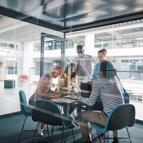 Laughing team of diverse businesspeople talking together during a meeting in a glass walled boardroom of a modern office